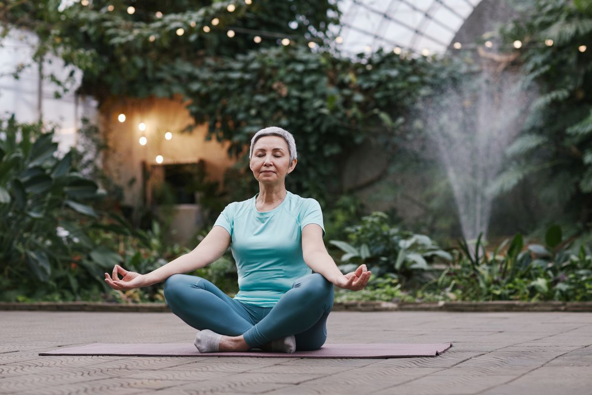 An older woman doing calm balance and breathing work outdoors.