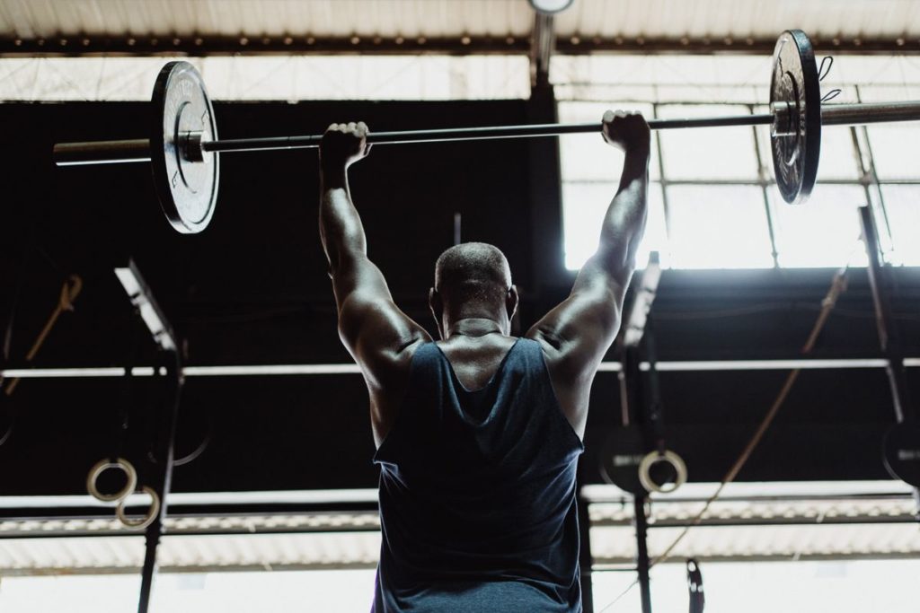 An athlete pressing a barbell overhead, a compound lift that anchors both full body and split routines