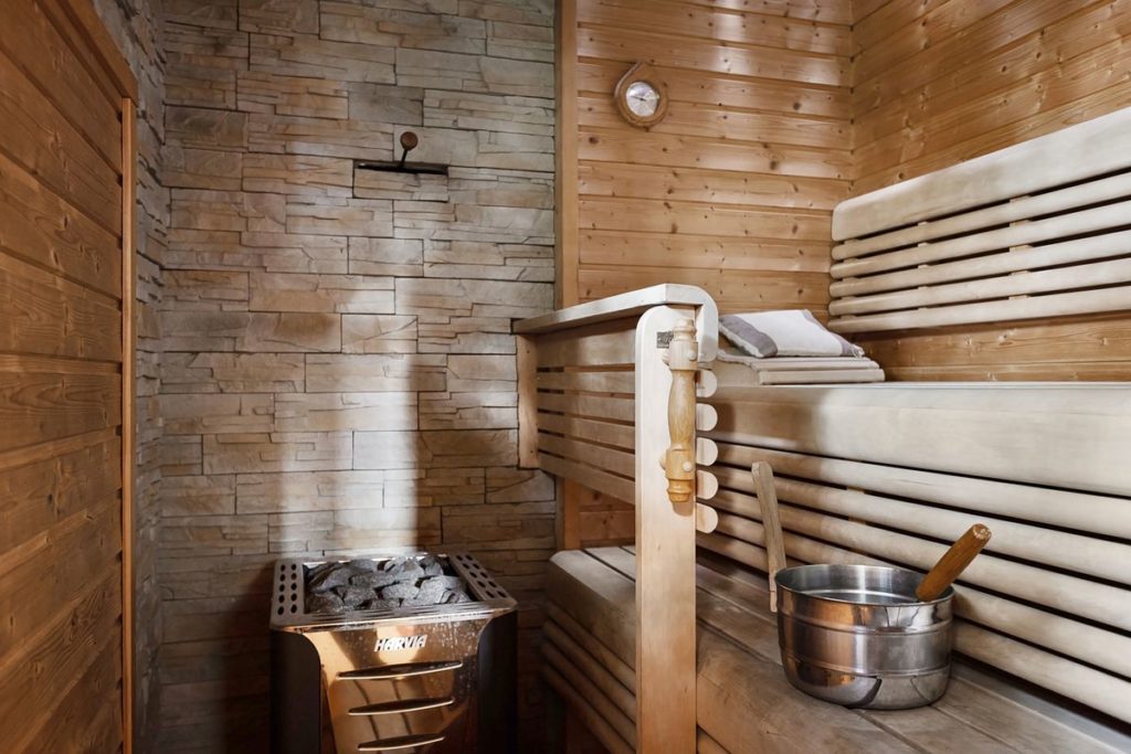 Modern home sauna interior with light wood benches and a stone wall