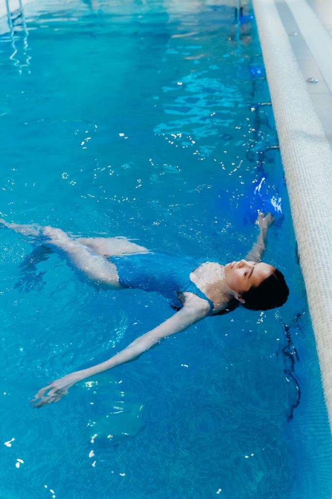A person floating calmly in a pool, the offloaded, gentle water work suited to returning after injury
